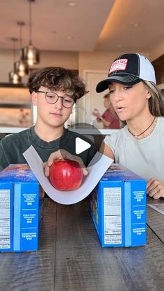 two people sitting at a table with boxes and an apple