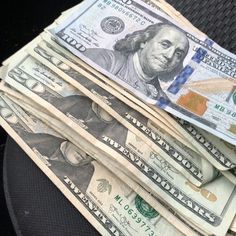 a stack of twenty dollar bills sitting on top of a black seat cushion in the back of a car