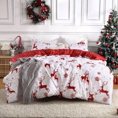 a bed covered in red and white sheets next to a christmas tree with wreaths