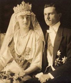 an old black and white photo of a man and woman dressed in wedding attire, sitting next to each other