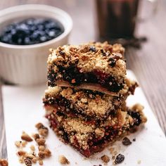 three pieces of dessert sitting on top of a white napkin next to a bowl of blueberries