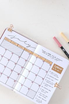 an open planner with markers and pencils next to it on a white table top