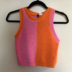 an orange and pink tank top hanging on a hanger next to a white wall