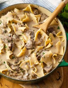 a skillet filled with pasta and meat in gravy on top of a wooden cutting board