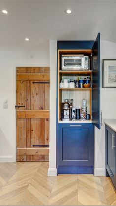 a kitchen with wooden floors and blue cabinets in the center, along with an open door leading to another room