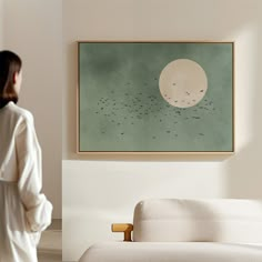 a woman standing in front of a painting on the wall next to a white couch