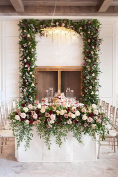 a table with flowers and greenery on it in front of a chandelier