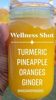 a person holding up a jar of orange juice with the words turmric pineapple ginger on it