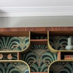 an art deco bookcase with books and vases on it's shelves in front of a wallpapered background