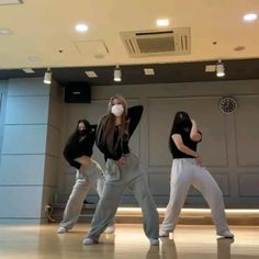 three women in grey pants and masks are dancing on the floor with their hands behind their backs