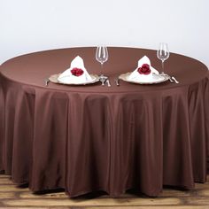 two wine glasses sitting on top of a round table with red roses in the center