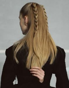 a woman with long blonde hair wearing a black dress and braiding her hair into a pony tail