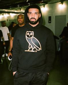 a man in a black hoodie with an owl on it's chest and his hands in his pockets