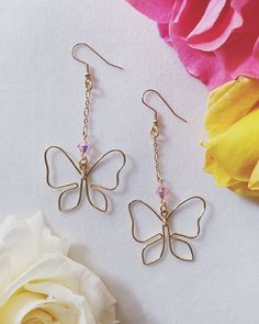 a pair of butterfly earrings sitting next to a flower