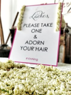 a sign that says please take one and adorn your hair on the table with flowers around it