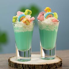 two glasses filled with ice cream and candy on top of a wooden table next to each other