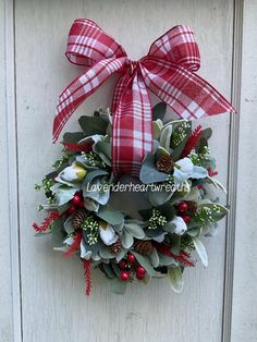 a red and white christmas wreath hanging on a door with holly, pine cones, berries and ivy