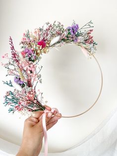 a person is holding a flower wreath with pink and purple flowers on it, while the other hand holds a ribbon