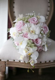 a bridal bouquet sitting on top of a chair with pink roses and white orchids