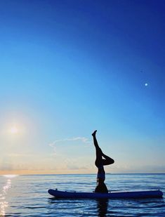 a person on a surfboard in the ocean doing a handstand yoga pose