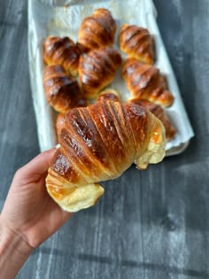 a person holding up a croissant in front of some other pastries on a tray