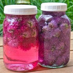 two jars filled with purple flowers sitting on top of a wooden table next to each other