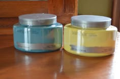 two jars of yellow and blue paint sitting on top of a wooden table next to each other