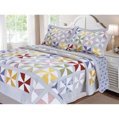 a bed with a colorful quilt on top of it next to a white dresser and window