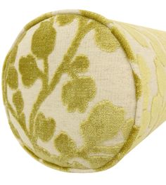 a green and white flowered pillow on top of a white surface with a light yellow background