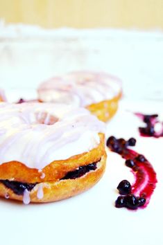 two glazed donuts with white frosting and blueberries on a plate next to other pastries