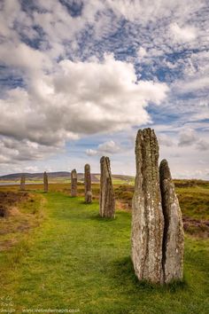 several large rocks in the middle of a grassy field under a cloudy blue sky with white clouds