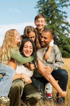 a group of people sitting on top of each other in a field with trees behind them