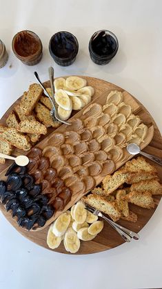 an assortment of breads, fruit and jams on a wooden platter with spoons