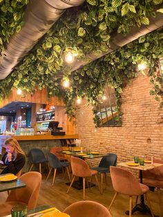 a woman sitting at a table in a restaurant with lots of green plants hanging from the ceiling