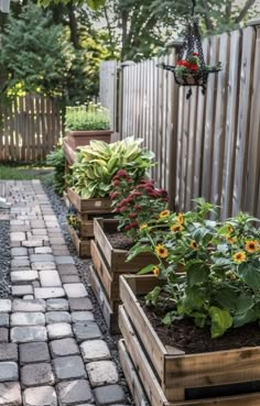 several wooden planters filled with plants on a brick walkway in a backyard area next to a fence