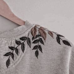 a close up of a shirt with leaves embroidered on the front and back, hanging from a wooden hanger