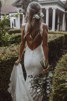 a woman in a white wedding dress walking down a path with flowers in her hair