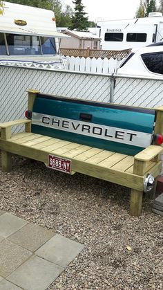 a bench that is sitting in the gravel next to a fence with a chevrolet license plate on it