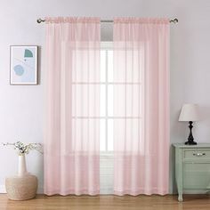 a pink curtain hanging on the side of a window next to a dresser and lamp