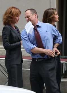 two women and a man are standing in front of a car talking to each other