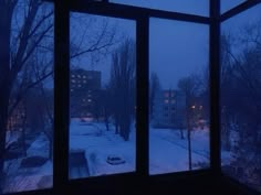 an open window looking out onto a snowy street at night with cars parked in the snow