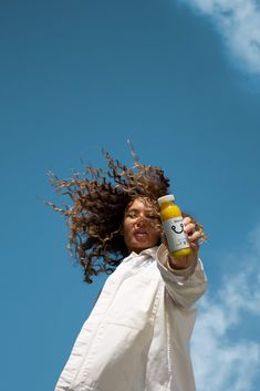 a woman holding up a bottle with her hair blowing in the wind on a sunny day