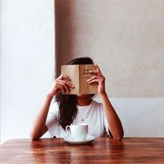 a woman sitting at a table with a book and coffee cup in front of her