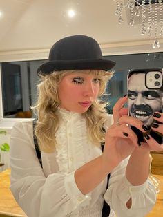 a woman taking a selfie in front of a mirror wearing a hat and holding a cell phone