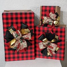 two red and black plaid boxes with gold bows on the top one has a present in it