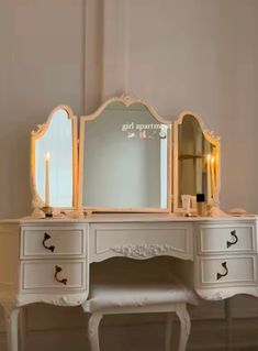 a white vanity with two mirrors on top of it and candles in front of it