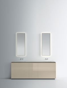 two sinks and mirrors in a white room with light from the mirror on the wall