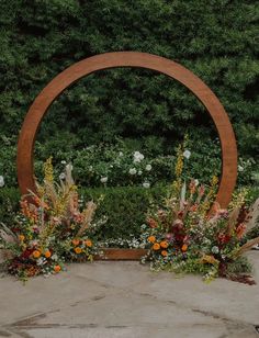 an outdoor ceremony with flowers and greenery on the ground in front of a circular wooden arch