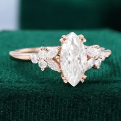 a ring with an oval cut diamond surrounded by smaller pear shaped diamonds on a green velvet surface