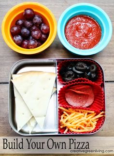 an open lunch box with grapes, crackers and pizza